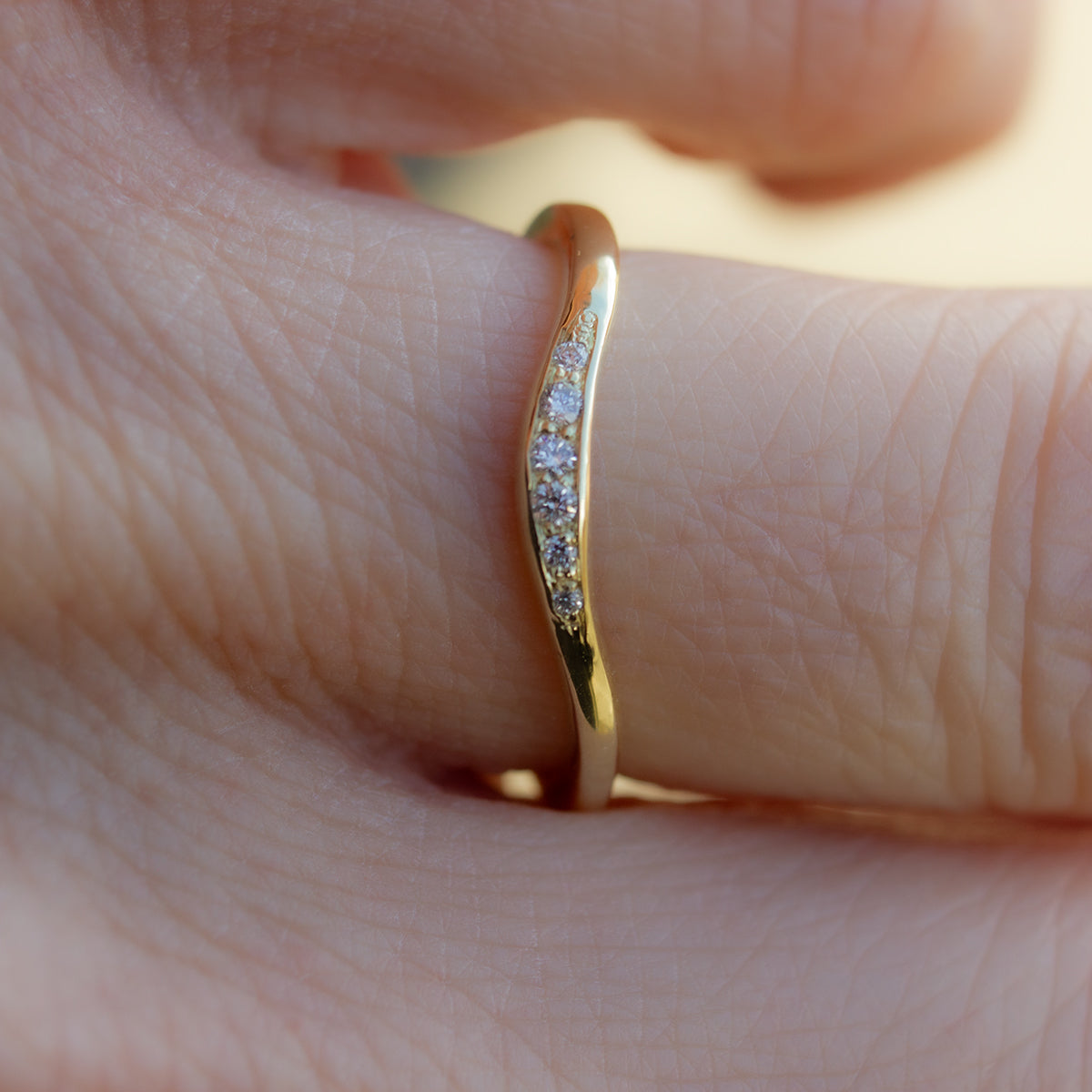 Curved shaped gold wedding band with pavé set white diamonds