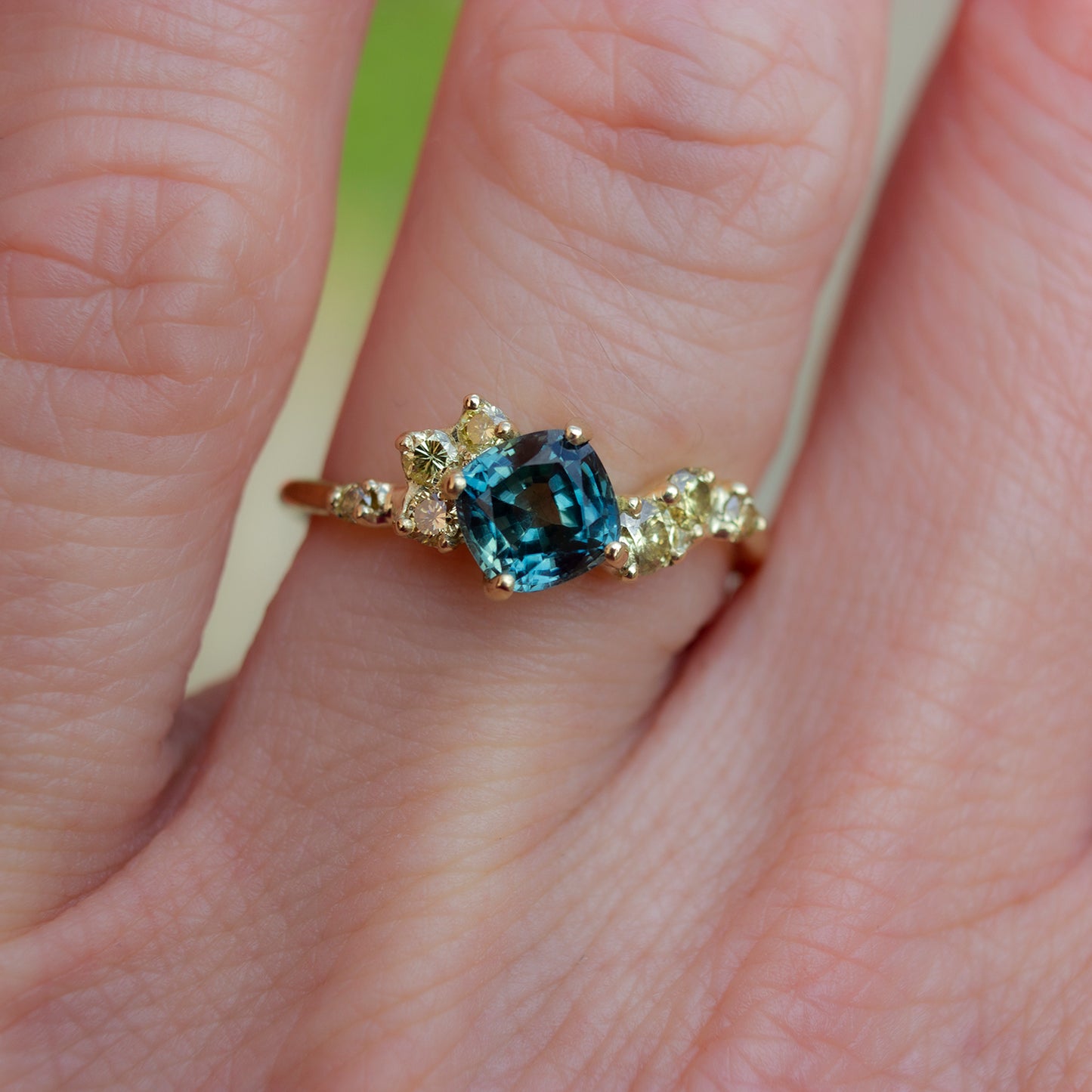 Beautiful, organically shaped ring featuring teal cushion cut sapphire surrounded with asymmetrically scattered yellow diamonds.