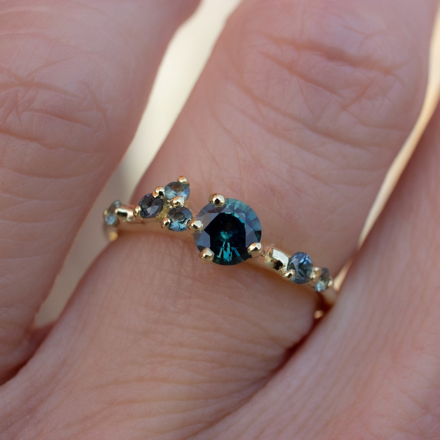 Asymmetrical, delicate ring featuring beautiful teal sapphires scattered along a gold band.
